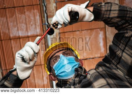 Electrician Worker At Work Replaces The Lamp Holder Protected By Helmet, Safety Goggles And Gloves; 