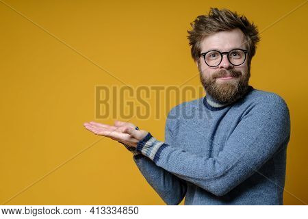 Benevolent Shaggy Man In A Knitted Sweater Makes A Gesture With Hands, Pointing At Something. Copy S