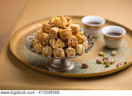 Baklava and arabic black coffee presented in a golden tray with few pistachio nuts. Beautiful photo of Turkish or Mediterranean sweet served with coffee.