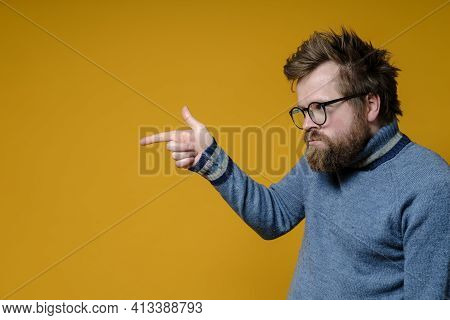Offended, Embittered Shaggy, Bearded Man With Glasses And A Sweater Points Finger At Someone With Di
