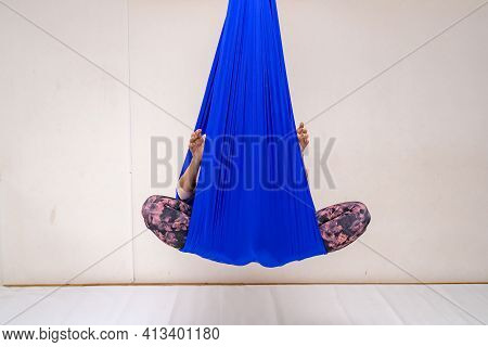 A Young Woman Poses While Doing Anti-gravity Aerial Yoga In A Blue Hammock On A White Background.