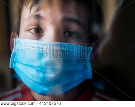 Boy With A Medical Mask Looks Sadly Out Of The Window During His Confinement Because Of Convid 19