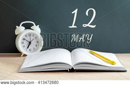 May 12. 12th Day Of The Month, Calendar Date. White Alarm Clock, An Open Notebook With Blank Pages, 