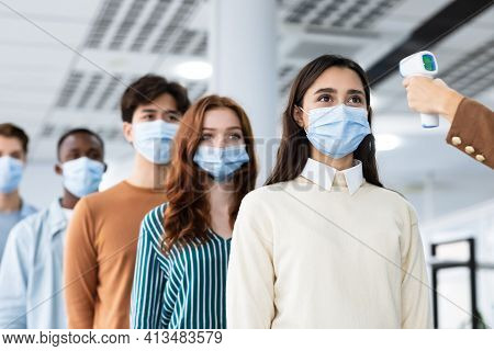 Woman With Contactless Thermometer Cheking Multiracial People Temperature In Queue