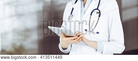 Unknown Woman Doctor Iusing Tablet Computer In Her Hands, While Standing In Clinic. Medicine Concept