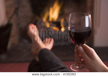 Nohy oteplování na krb s rukou drží víno