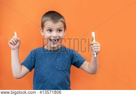 Boy Without Milk Upper Tooth In Blue T-shirt Holds Toothbrush In Hand On The Orange Background.