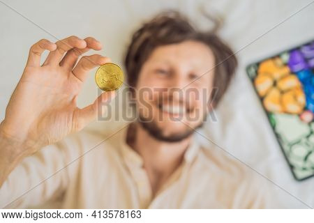 Young Man, A Digital Artist, Creates Digital Art On A Tablet At Home And Shows A Coin With The Inscr
