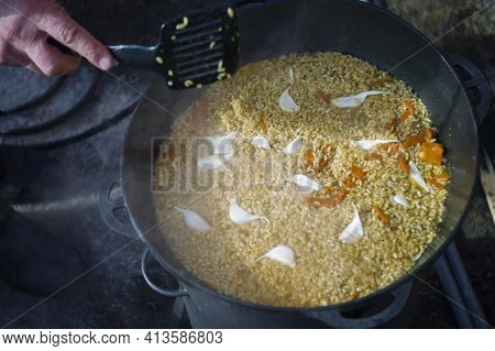 Garlic In Pilaw And A Hand With Ladle, Outdoor Close Up, Slightly Defocused Shot