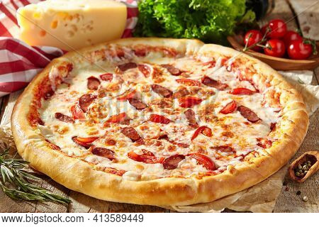 Spicy Sausage Italian Pizza with tomato, mozzarella cheese, sausage slice. Homemade pizza on baking paper with food ingredients on wooden table. Fast food or junk food pizza dinner rustic style