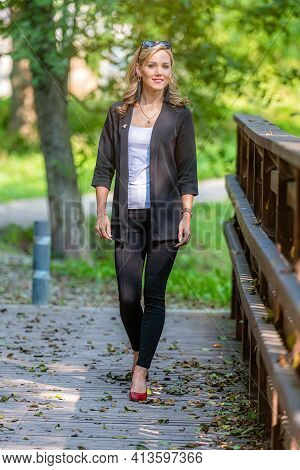 Young Positive, Smiling, Legant Woman Walks On A Wooden Footbridge On A Sunny Autumn Day