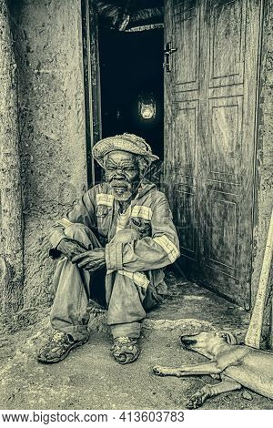 Portrait of an African old man sitting with his dog in the door in a village in Africa, night scene paraffine lamp in the back