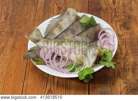 Raw Carcasses Of Notothenia Fish Without Of The Heads, Greens And Round Slices Of Red Onion On Dish 