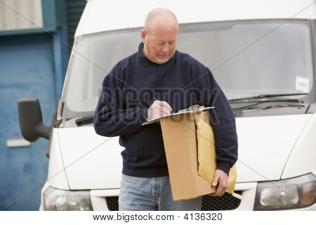 Deliveryperson permanente con escritura Van en portapapeles sosteniendo la caja sonriendo
