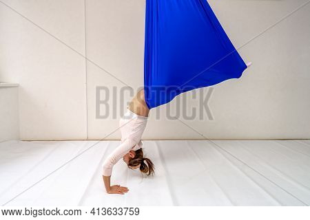 A Young Woman Poses While Doing Anti-gravity Aerial Yoga In A Blue Hammock On A White Background.