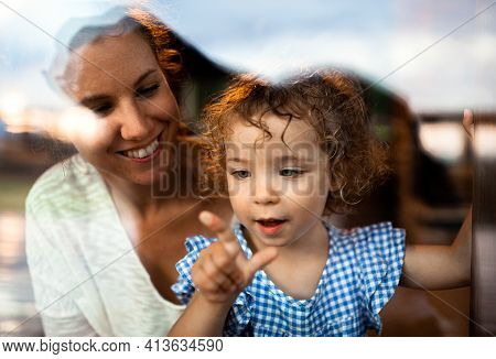 Small Girl With Mother By Window, Holiday In Nature Concept. Shot Through Glass.