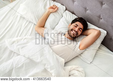 Wellslept Arab Man Waking Up And Smiling, Enjoying Good Morning In Bed