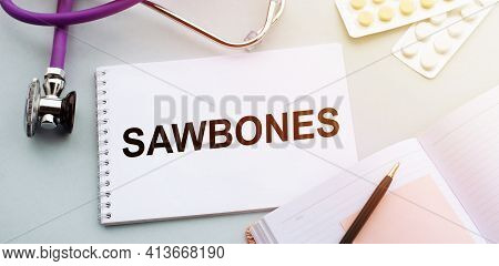 Stethoscope, Pills And Notebook With Sawbones Word On Medical Desk.