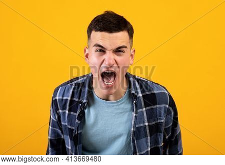 Frustrated Young Guy Shouting In Anger, Expressing His Fury Over Orange Studio Background. Negative 
