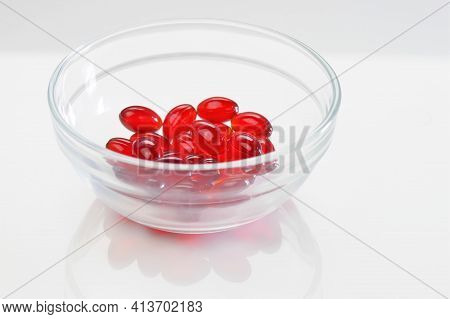 Krill Oil Capsules. Red Gelatin Capsules With Krill Oil In A Glass Transparent Cup On A White Backgr