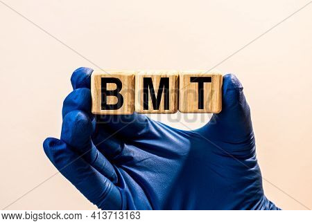 The Word Bmt Which Is Made From Wooden Cubes. Hands In A Blue Glove. Isolated On White Background