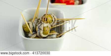 The Traditional Spanish Appetizers Of Olives, Tomatoes And Anchovies In A White Ceramic Bowls