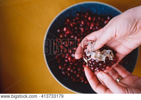 Woman Deseeding Fresh Red Pomegranate On Yellow Table