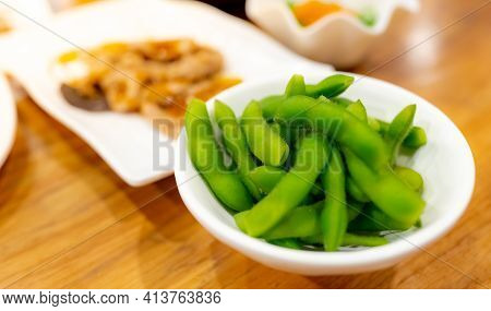 Edamame Or Green Soybeans Blanched In White Bowl On Wooden Table At Japanese Restaurant. Pods Of Gre