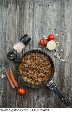 Fried Chicken Liver With Onions And Carrots In A Black Pan On A Wooden Textured Table. The Pan Is Vi