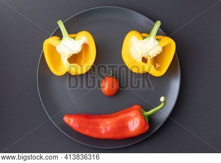 Capia Pepper, Cherry Tomato And Two Slices Of Yellow Pepper Making Face On Dark Plate Placed On Blac