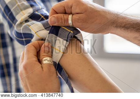 Unrecognizable Male With Hairy Hands Rolling Sleeve Of Checkered Shirt On Arm Of Crop Female