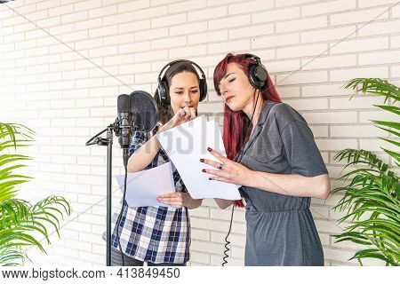 Young Women In Headphones Discussing Script While Standing Near Microphone Against Brick Wall In Fil