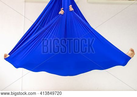 A Young Woman Poses While Doing Anti-gravity Aerial Yoga In A Blue Hammock On A White Background.