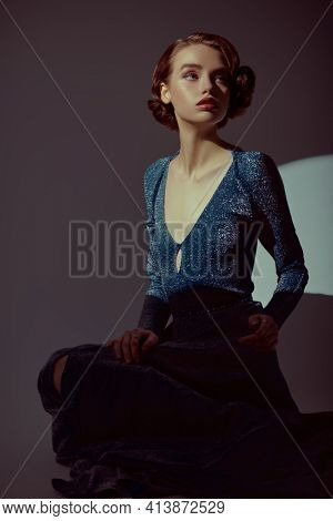 Stunning young woman in a dark silvery dress and with hair and makeup in the style of the 20s posing in dark room. Art fashion portrait. 