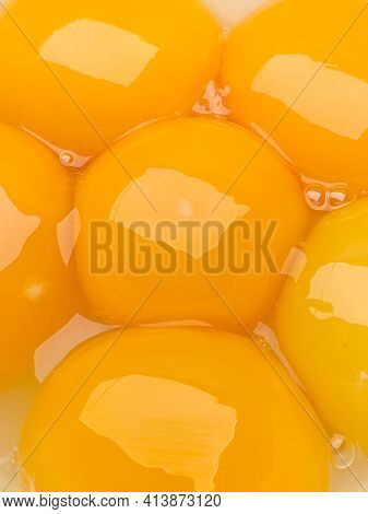 Six bright yellow raw egg yolks in a bowl, close-up.