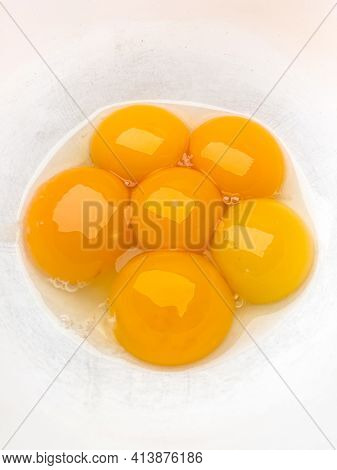 Six bright yellow egg yolks in a white bowl.