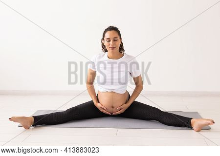 Young Flexible Pregnant Woman Doing Gymnastics On Rug On The Floor On White Background. The Concept 
