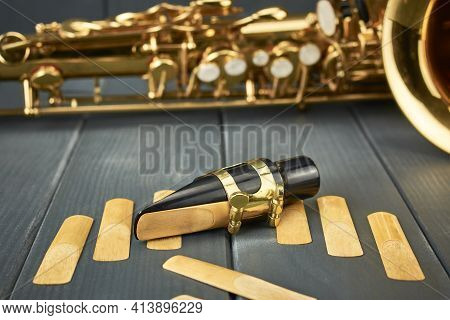 Saxophone Mouthpiece And Reed With Clamp And Gold Hardware Along With Spare Reeds On Gray Wooden Bac