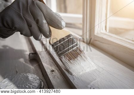 Painting Wooden Window With White Color. Brush In Hand With Grey Glove. Ronoveation And Restauration