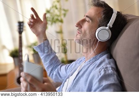 Detail Of Man Sitting On The Sofa At Home Listening To Music Concentedly From A Mobile Phone With Wh