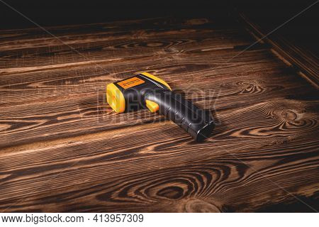 Yellow-black Pyrometer On A Wooden Background. A Device For Non-contact Temperature Measurement. Stu
