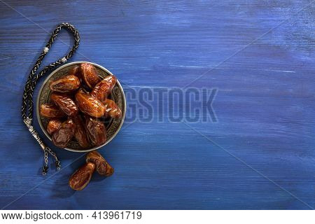 Silver plate with dates and  tasbih (misbaha) on old  dark blue wooden table. Ramadan background. Flat lay.  Selective focus.