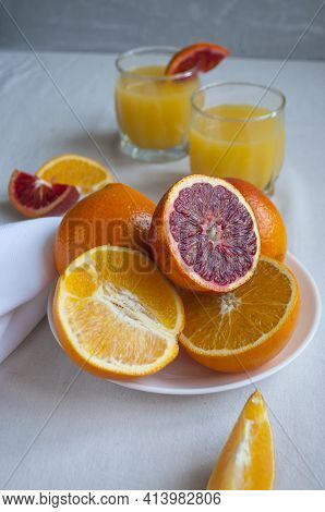 Sweet And Juicy Blood Oranges And Oranges, Whole And Cut On A White Plate And Gkasses Of Fresh Orang