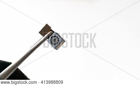 Close-up On The Mobile Phone Camera Module. Close-up Tweezers Or A Clip Holds The Smartphone Lens In