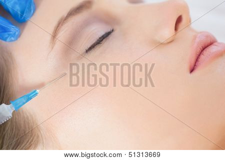 Surgeon in bright operating room making injection on woman's crows feet 