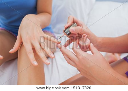 Friends sitting on bed and painting each other nails at sleepover