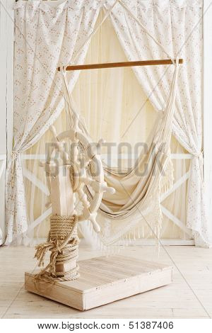 Beautiful wooden ship wheel in room decorated with curtains.