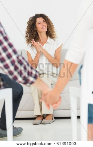 Pleased therapist looking at reconciled couple holding hands at therapy session