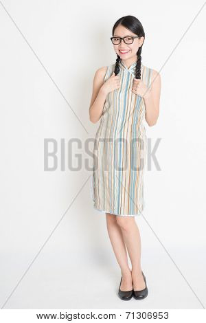 Portrait of old-fashioned Asian Chinese girl in traditional cheongsam or qipao dress smiling, full length standing on plain background.