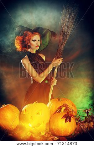 Beautiful red-haired witch casts a spell over pumpkins. Halloween.